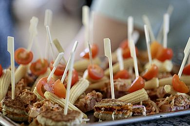 Als Häppchen werden gefüllte Hackfleischbällchen angeboten, die mit Tomate und kleinen Mini-Maiskolben garniert sind.