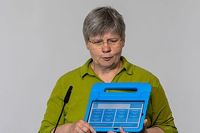 Susanne Wagner ist Leiterin der Abteilung Forschung und Entwicklung der BBW-Leipzig-Gruppe. Vor ihr hellgrünes Hemd hält sie ein hellblaues LSI.J-Sprachtest-Tablett.