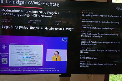 Ein Bildschirm im Backstage-Bereich gibt die "Regie-Ansicht" für den AVWS-Fachtag wieder. Mit weißer Schrift auf schwarzem Bildschirm stehen Information zum Ablaufplan wie Moderationsauftakt und Details wie Zeitdauer des Beitrages. 