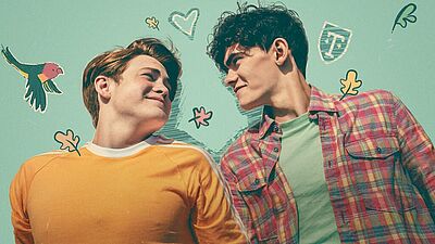Banner der Serie "Heartstopper": Zwei Männer (Mitte 20) schauen sich an, der linke trägt einen gelben Pullover und hat dunkelblonde Haare, der rechte trägt ein rot-grün-kariertes Hemd und hat dunkle kurze Haare.