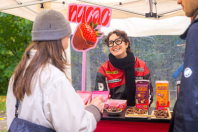Stand mit veganer Schokolade. Verkäufer*in lächelt Kund*innen an