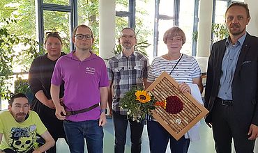 Gruppenfoto mit Werkstattmitarbeitenden, der Preisträgerin, dem Bereichsleiter und dem Hauptgeschäftsführer der BBW-Leipzig-Gruppe.