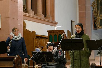 Mitglieder des inklusiven A-Capella-Ensembles Thonkunst tragen warme Kleidung und singen in einer Kirche.