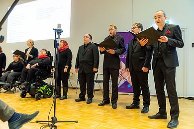 Das Vocalensemble Thonkunst singt ein Lied, die Mitglieder sind schwarz gekleidet und tragen rote Accessoires