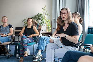 Sozialbürgermeisterin Dr. Martina Münch sitzt an einem Tisch und blickt aufmerksam eine Person an, die unscharf von hinten zu sehen ist und vorne am Tisch sitzt. Die Person, die von hinten zu sehen ist, hält mehrere beschriebene, farbige Karteikarten in der Hand. Auf dem Tisch liegen bereits mehrere weitere Karteikarten sauber angeordnet.
