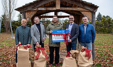 Übergabe des Spendenchecks an Tom Spindler von den Stationären Erziehungshilfen am BBW. 5 Männer mit Jutesäcken mit großen roten Schleifen drum, die beiden in der Mitte halten den Spendencheck.