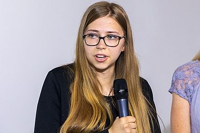 Emilie ist Auszubildende im Bereich Zahntechnik am Berufsbildungswerk Leipzig. Sie meldet sich bei der Gesprächsrunde zu Wort. Ihre langen hellbraunen Haare reichen bis zur Hüfte.