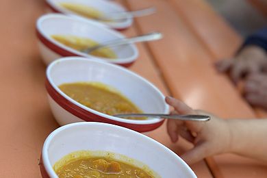 Auf einem Gartentisch stehen kleine Schüsseln mit Kürbissuppe. Eine Kinderhand greift nach einer der Schüsseln.