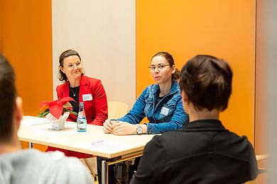 Zwei Personen sitzen an einem Tisch, im Vordergrund sieht man leicht verschwommen einen Zuhörer von hinten