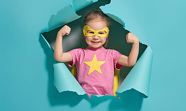 Mädchen als Superwoman verkleidet hinter einer Papierwand