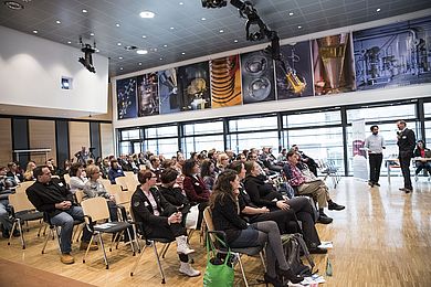 Viele Menschen sitzen in einem hellen, großen Raum während der Konferenz