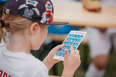 Ein Mädchen mit einer Karte, auf dem das Fingeralphabet der Deutschen Gebärdensprache abgebildet ist.