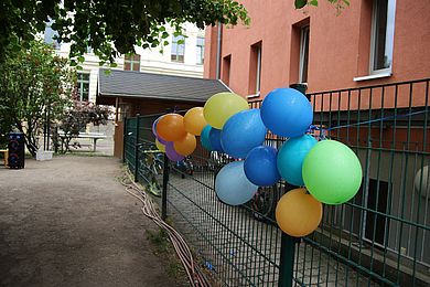 Bunte Luftballons in Blau, Grün, Orange und Gelb schmücken den Garten der Kita.