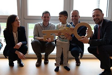 Ein Junge hält einen großen Holzschlüssel, neben ihm Erwachsene