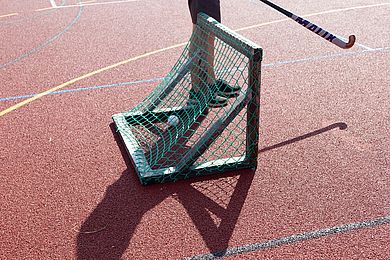 Ein Hockeyspieler steht mit Schläger vor ein Tor, in dem ein Ball zu sehen ist.