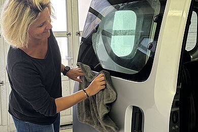 Eine Frau poliert mit einem weichen Tuch die rechte hintere Seite eines Autos. 