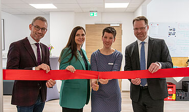 Vier Personen halten ein rotes Satin-Band. Von links: Prof. Dr. med. Fuchs, Claudia Rodegast, Lea Beuter, die die Schere angesetzt hat, und Bastian Schmiedel